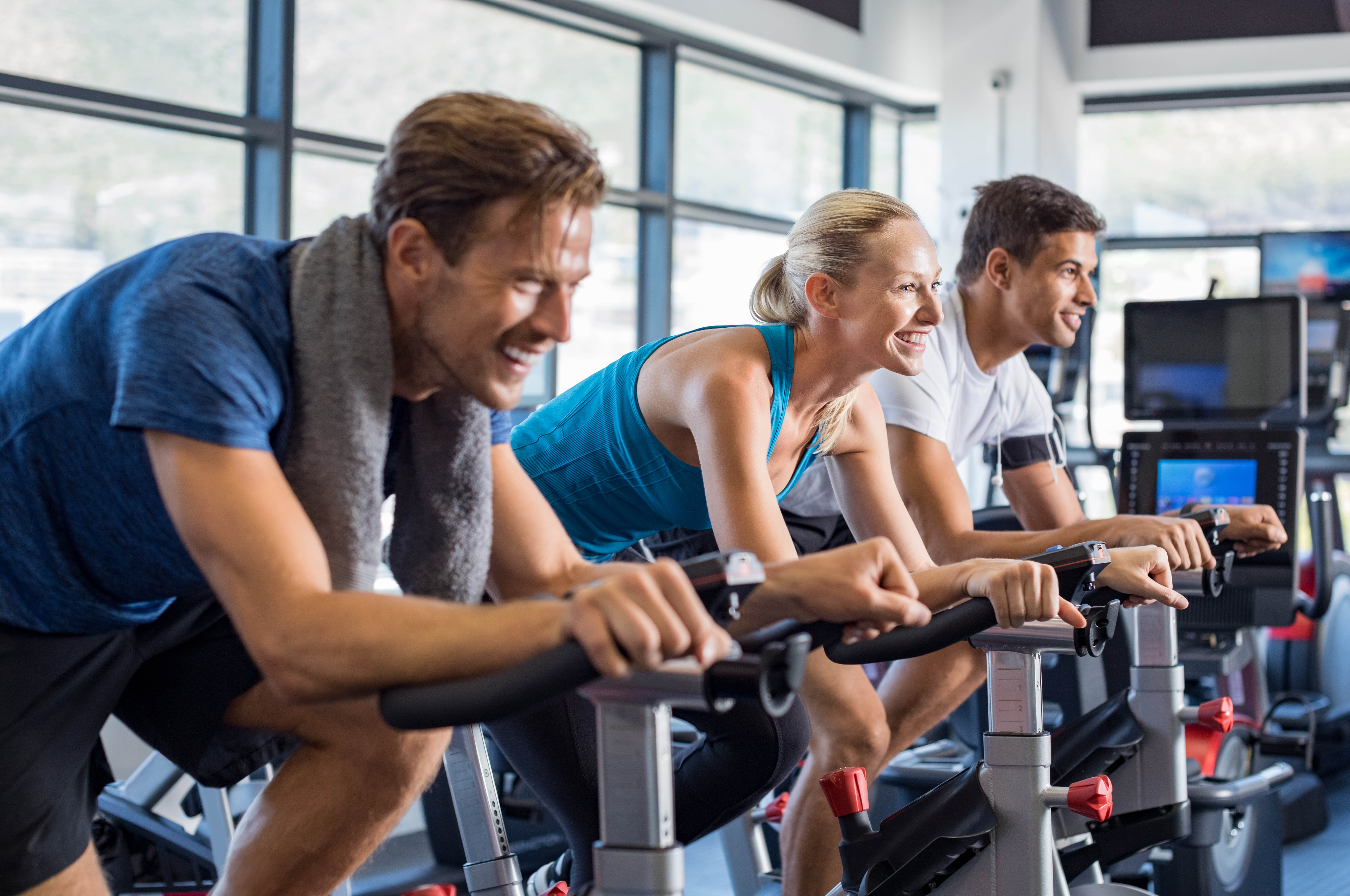Group of 3 young men and women smiling during a cycling class at a gym/fitness club Group of 3 young men and women smiling during a cycling class at a gym/fitness club